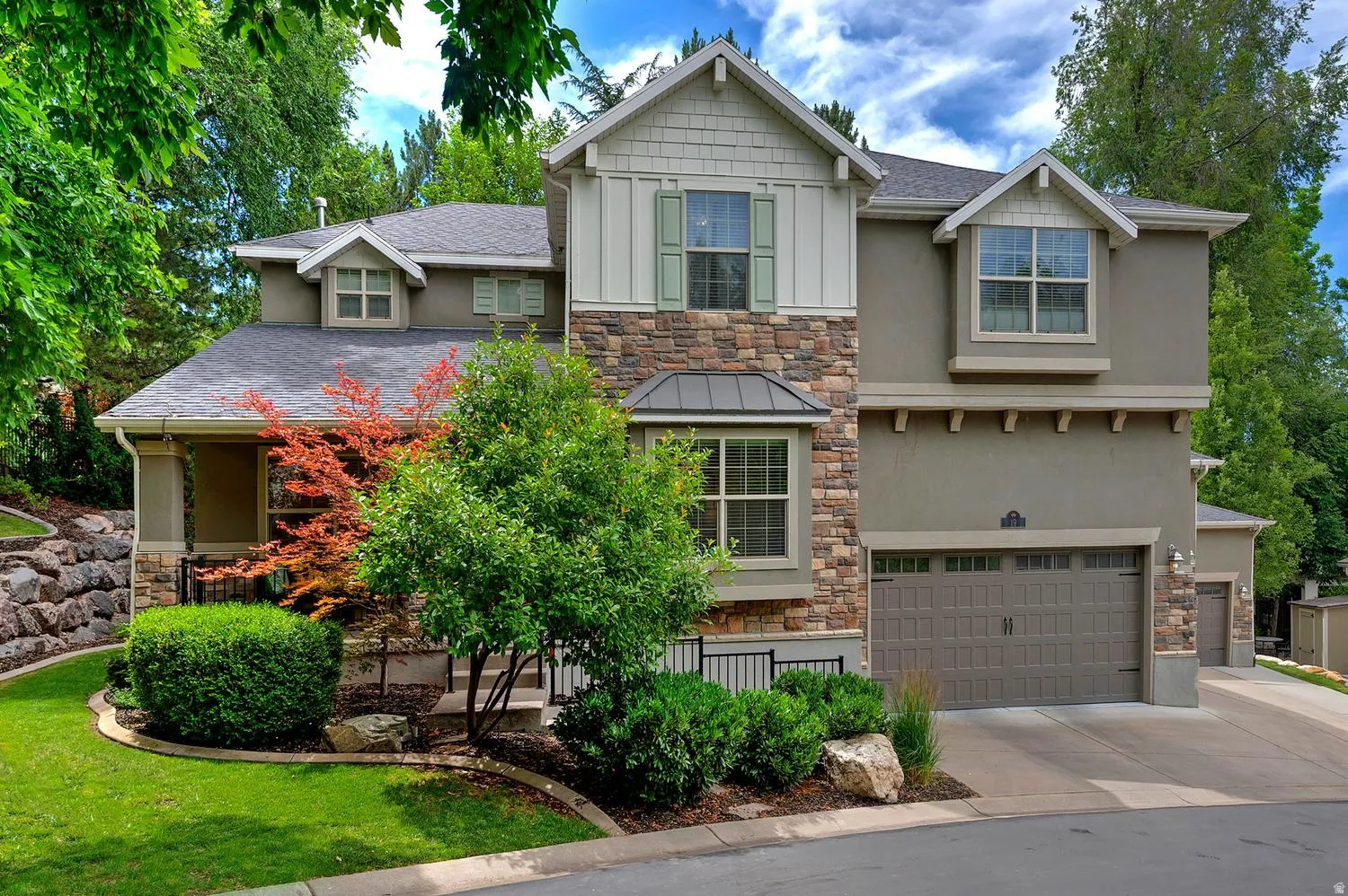 Multi-story exterior featuring a stone and stucco facade, a two-car garage, mature landscaping, and an additional single-car garage