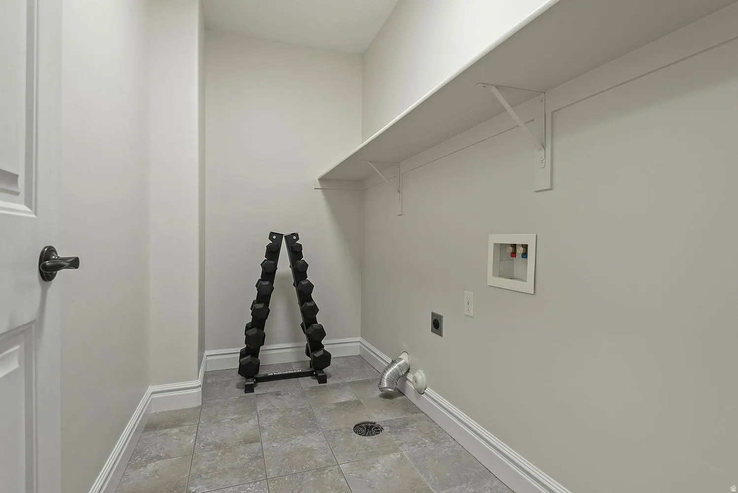 Laundry area featuring tile flooring, a utility sink drain, wall-mounted shelving, and plumbing hookups