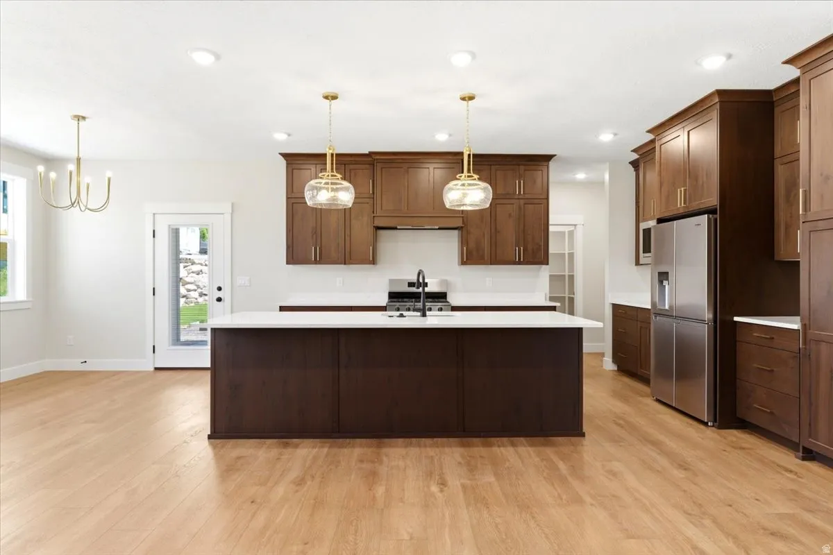 Expansive kitchen featuring a large central island, warm wood-finish cabinetry, stainless steel appliances, and contemporary pendant lighting,