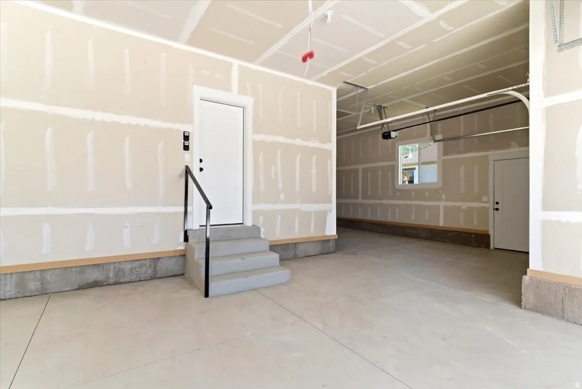Spacious, unfinished garage featuring concrete flooring, unpainted drywall, and an overhead garage door mechanism