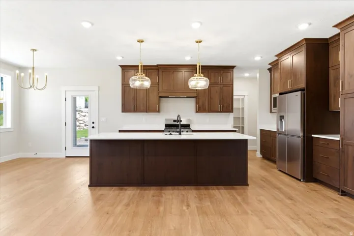 Expansive kitchen featuring a large central island, warm wood-finish cabinetry, stainless steel appliances, and contemporary pendant lighting,