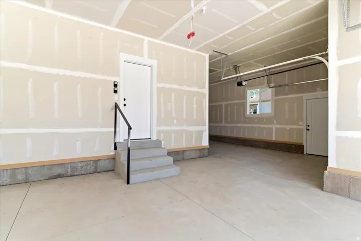Spacious, unfinished garage featuring concrete flooring, unpainted drywall, and an overhead garage door mechanism
