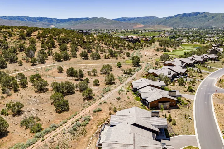 Community of contemporary homes with sloped rooflines, stone, and wood siding, bordered by natural terrain with scattered trees