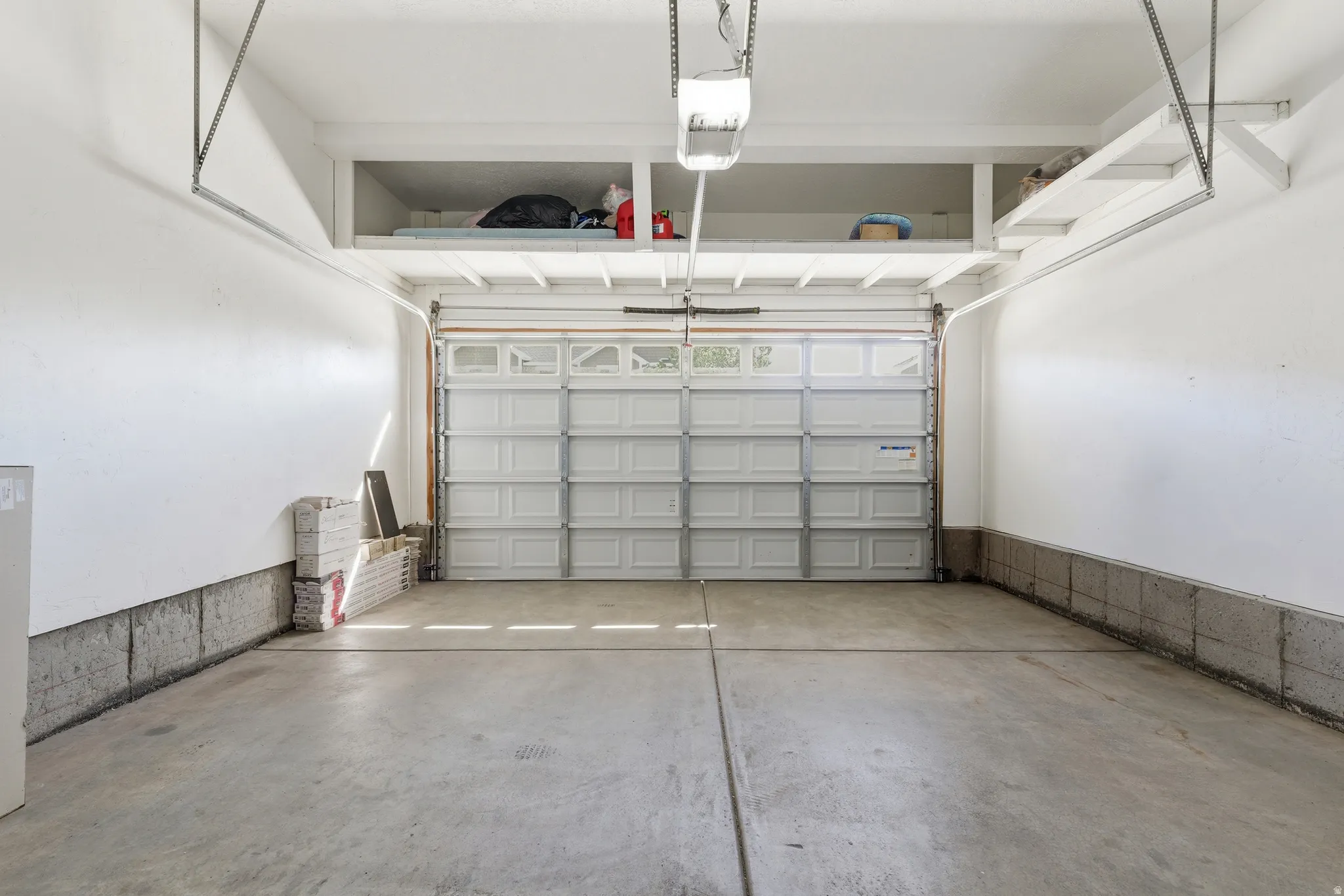 Attached garage featuring a sectional overhead door with upper window panels, a concrete floor, and overhead storage shelving