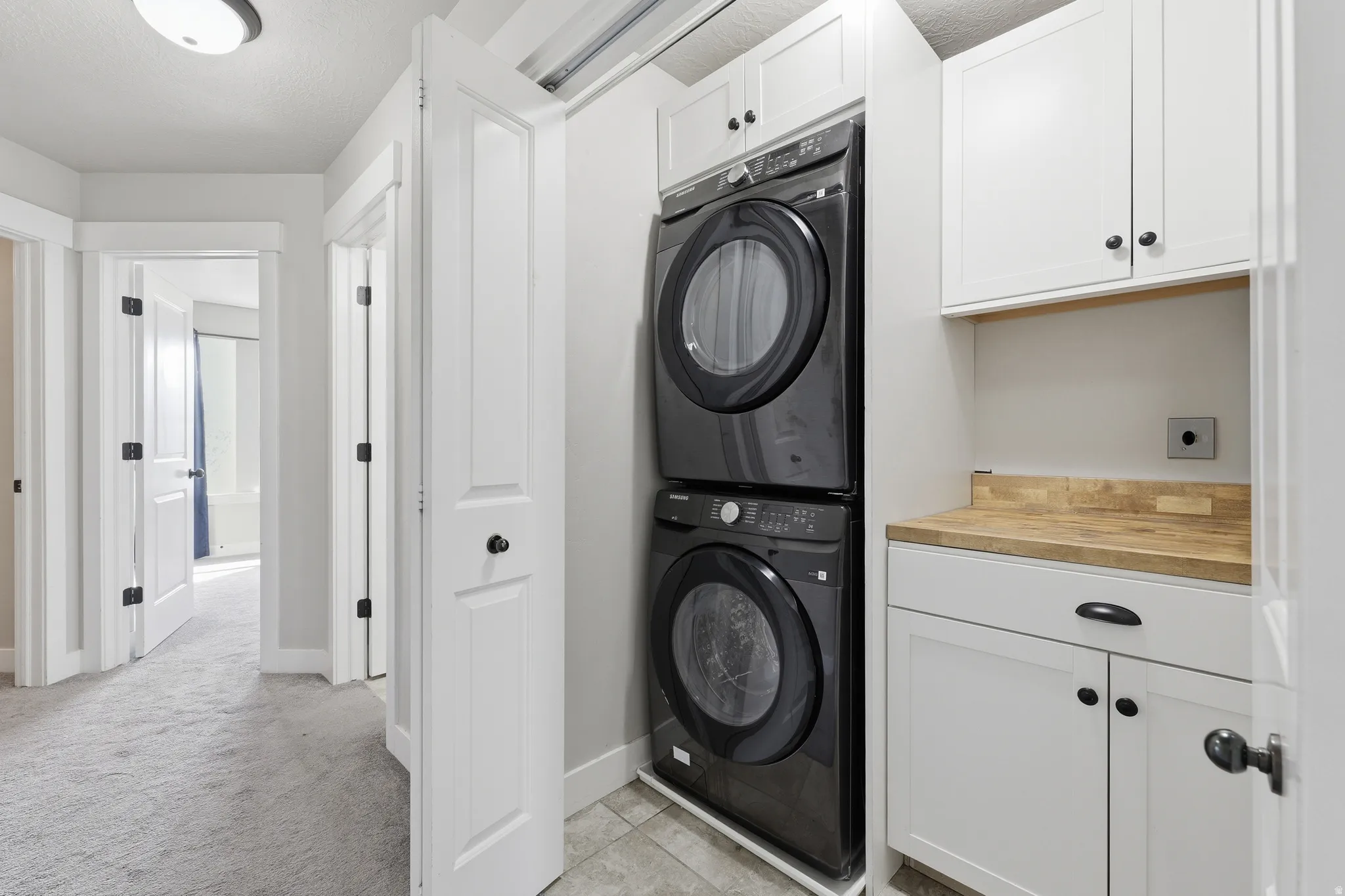 Dedicated laundry area featuring a stacked washer and dryer, white shaker cabinetry, and a wood-finish countertop