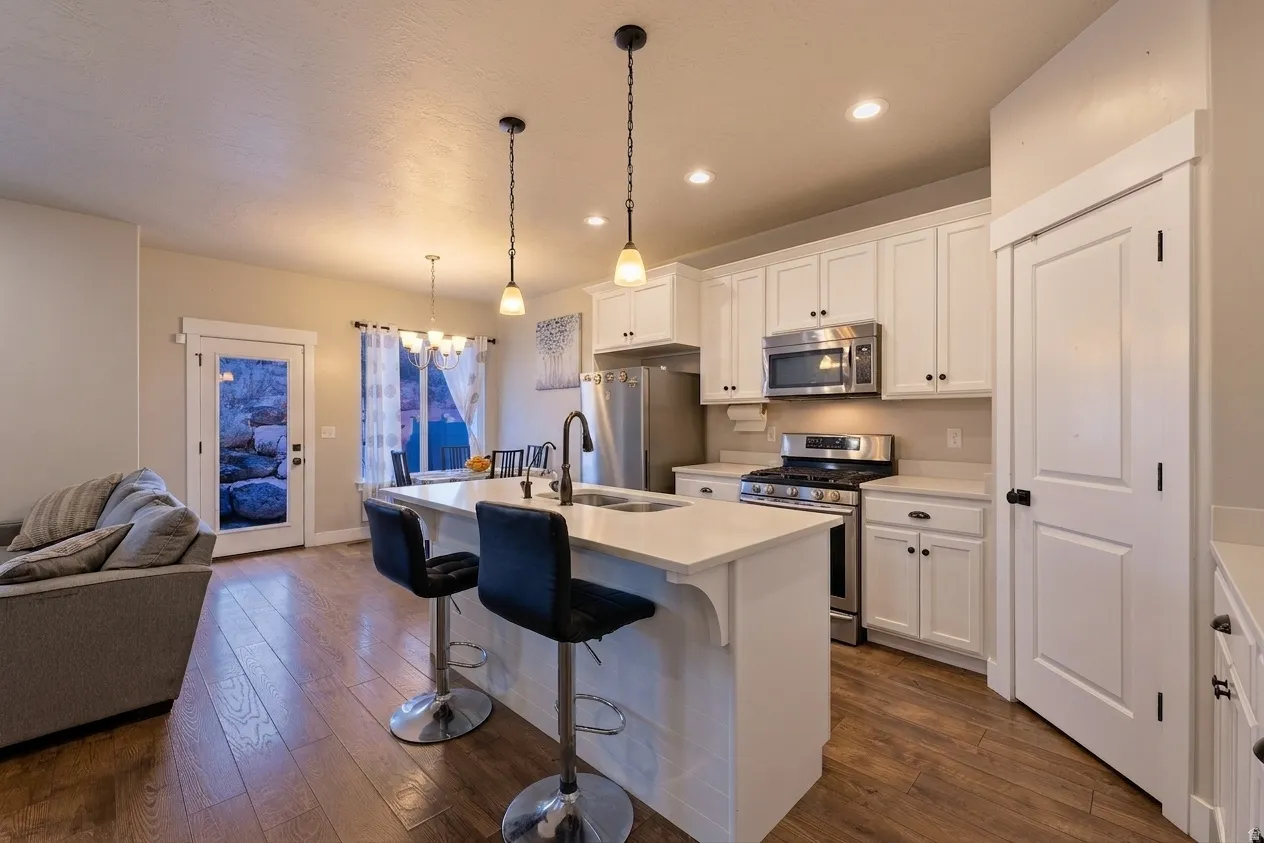 Modern kitchen featuring white cabinetry, stainless steel appliances, a center island with bar seating, pendant lighting, and wood-finish flooring