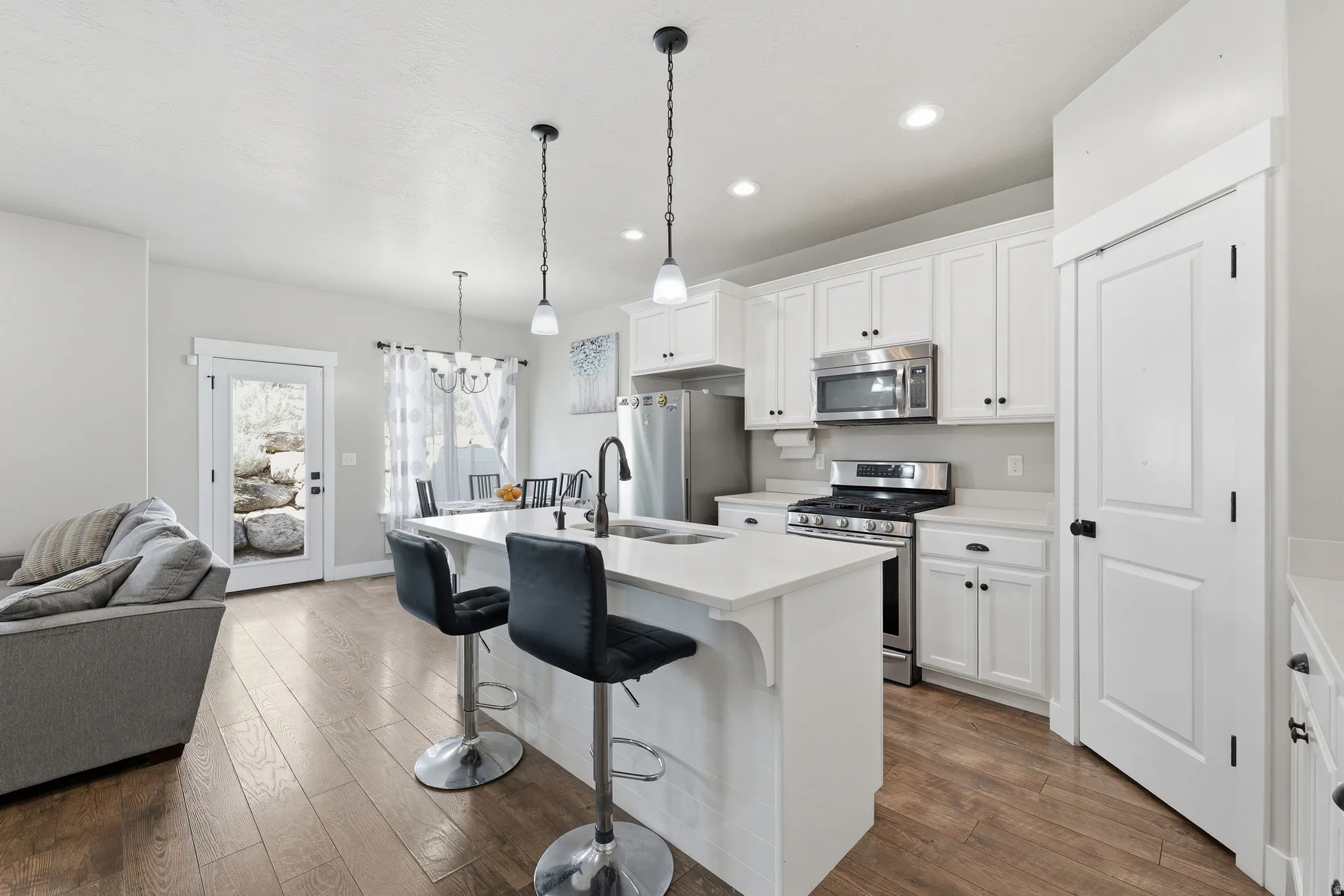 Open-concept kitchen featuring white cabinetry, stainless steel appliances, a center island with pendant lighting, and wood-finish flooring