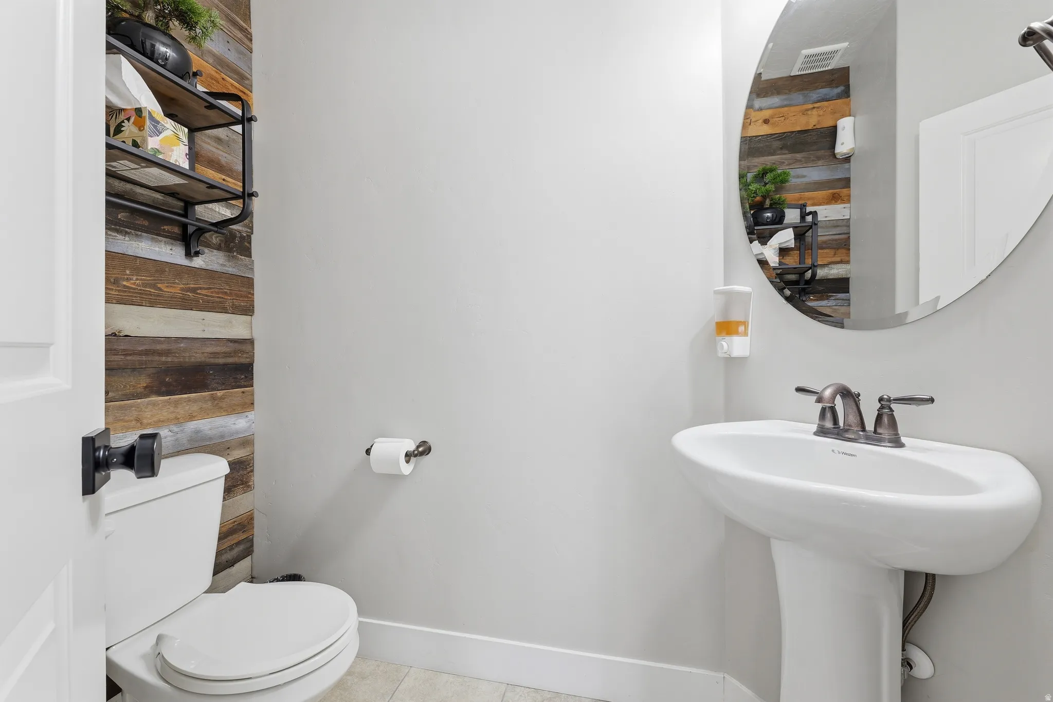 Pedestal sink with bronze-finish faucet, circular wall mirror, and wood-paneled accent wall
