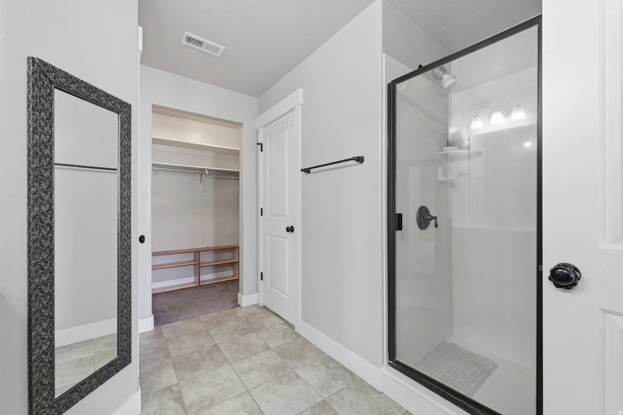 Bathroom featuring a glass-enclosed shower with matte black fixtures, tile flooring, and a walk-in closet with built-in shelving and hanging rods
