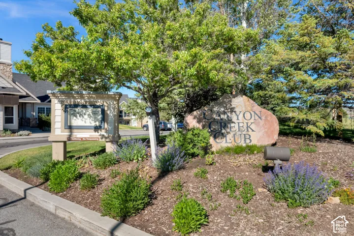 Landscaped entry featuring a large stone monument, decorative sign structure, and mature trees