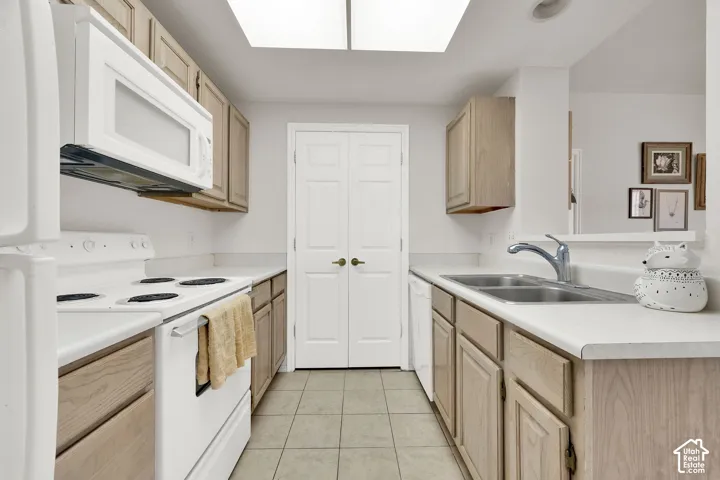 Galley kitchen featuring light wood-finish cabinetry, white appliances, and a dual basin stainless steel sink