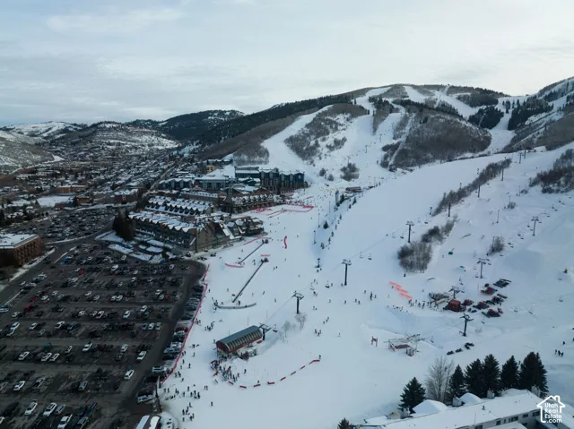 Aerial perspective showcasing a ski resort village nestled at the base of snow-covered mountains, featuring multiple ski runs, chairlifts, and a large parking area