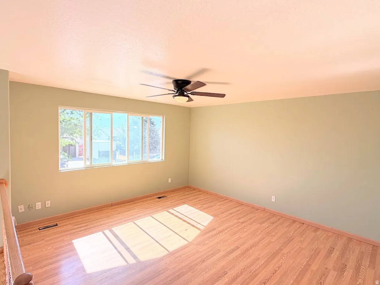 Spacious room featuring wood-finish flooring, a multi-pane window, and a ceiling fan with integrated lighting