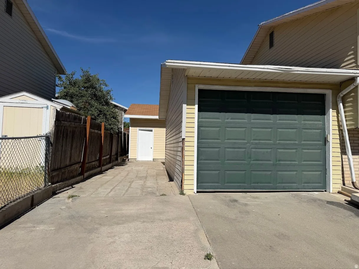 Detached garage with a paneled green door and light yellow siding