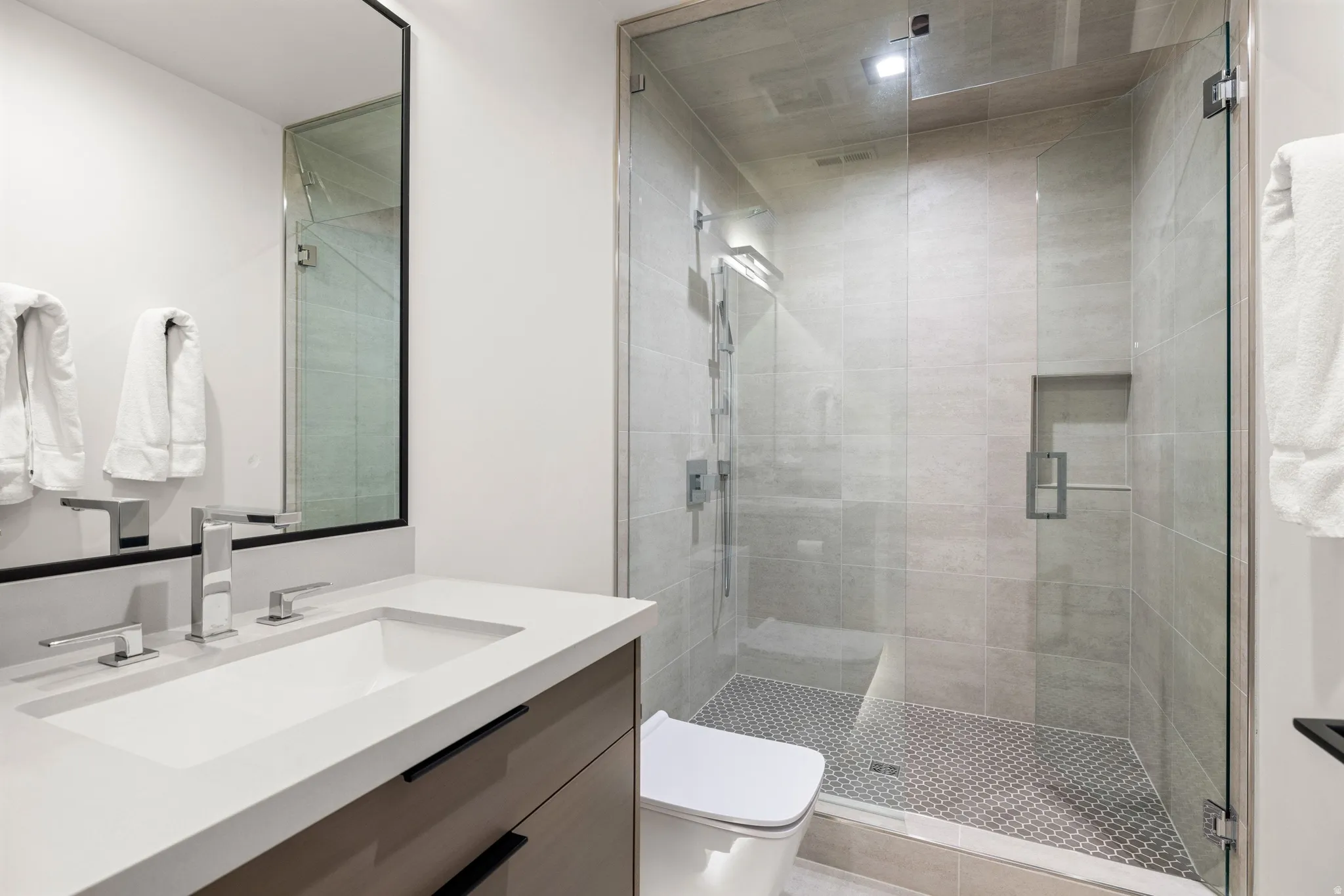 Contemporary bathroom featuring a frameless glass shower enclosure, integrated shower niche, and a wall-mounted rain shower head