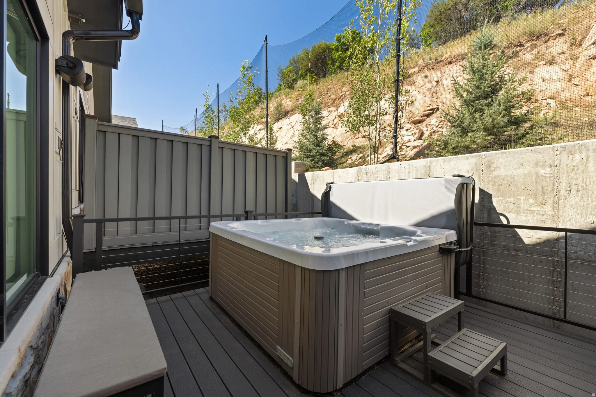 Outdoor patio featuring a built-in hot tub with cover, composite decking, and a low stone wall