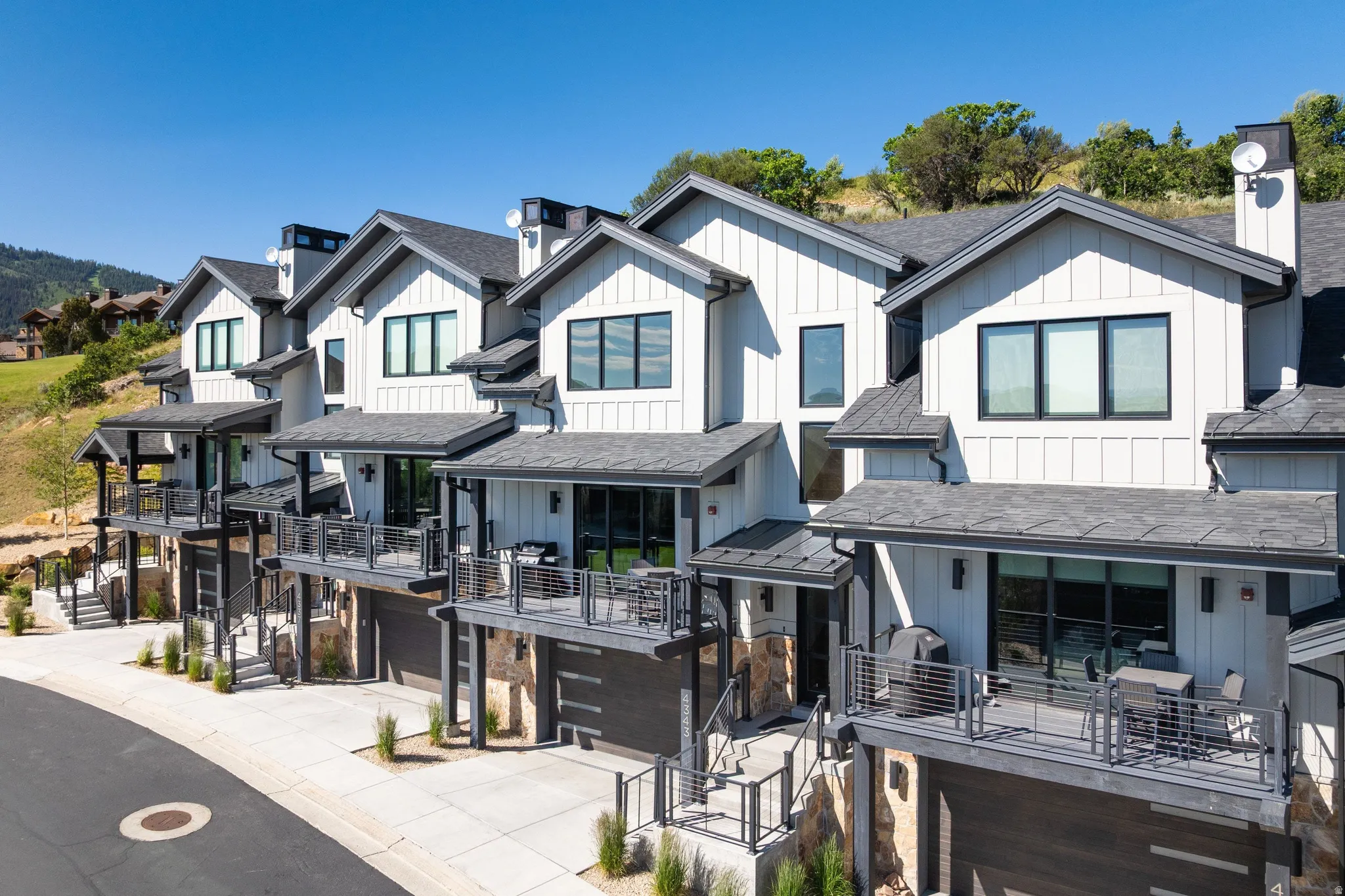 Modern townhome exteriors featuring white board and batten siding, dark trim, and individual balconies with metal railings
