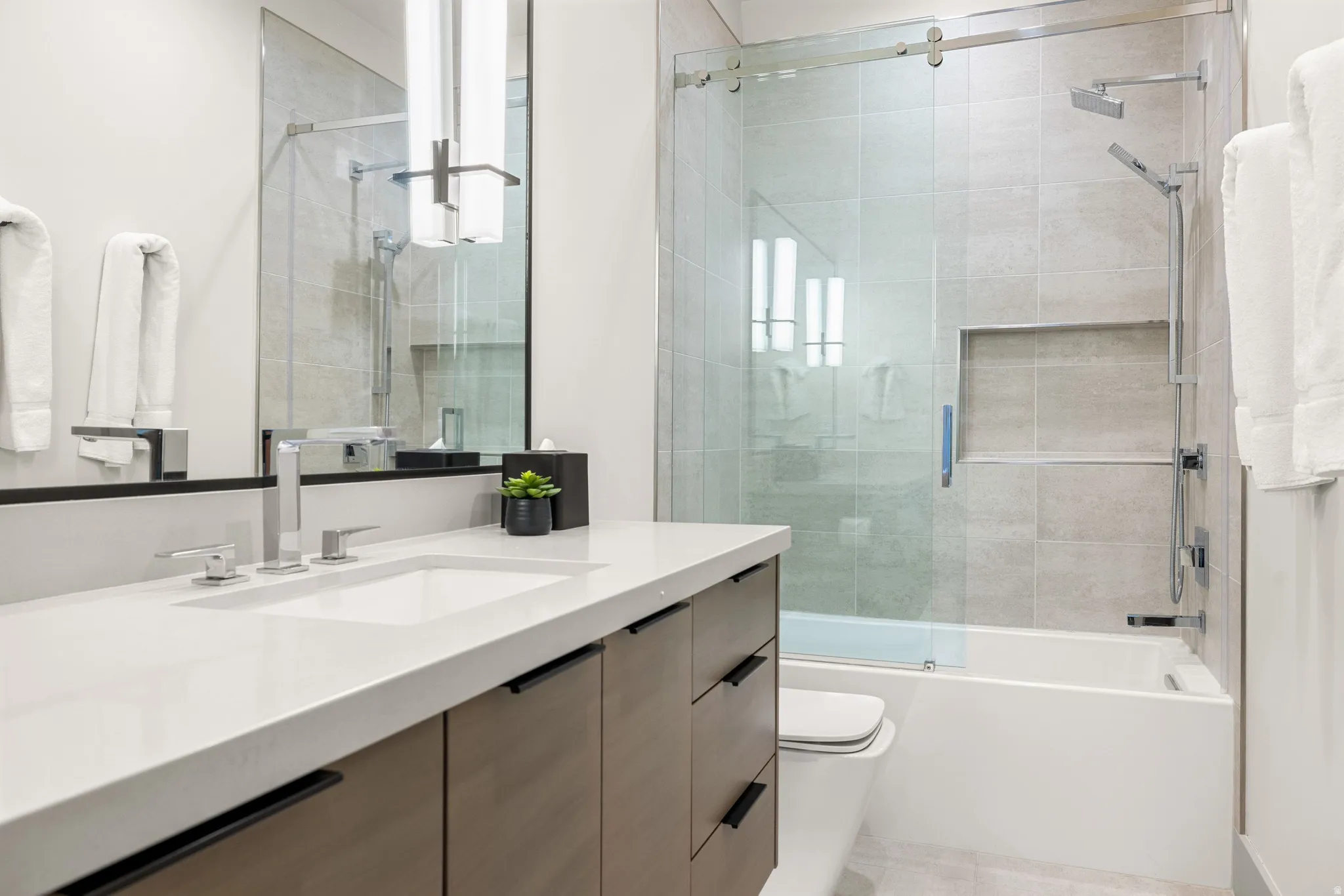 Contemporary bathroom featuring a vanity with wood-finish cabinetry, a white countertop with an integrated sink, and a chrome faucet