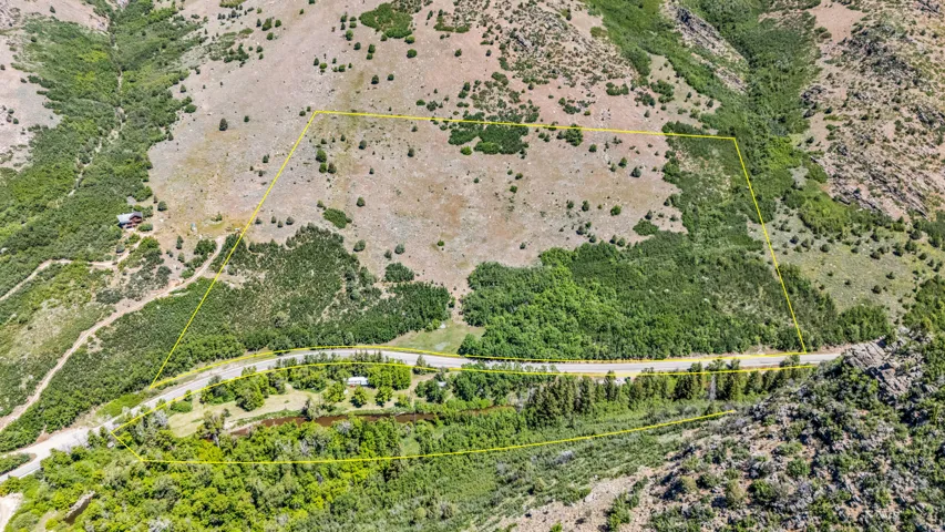 Expansive mountain property featuring varied terrain, mature trees, a visible roadway, and a natural watercourse