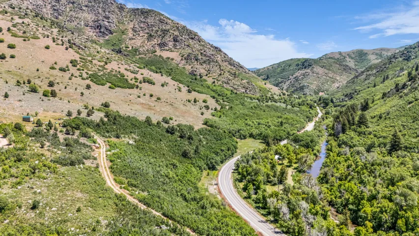 Expansive mountain terrain featuring a paved road, a winding river, and abundant green foliage