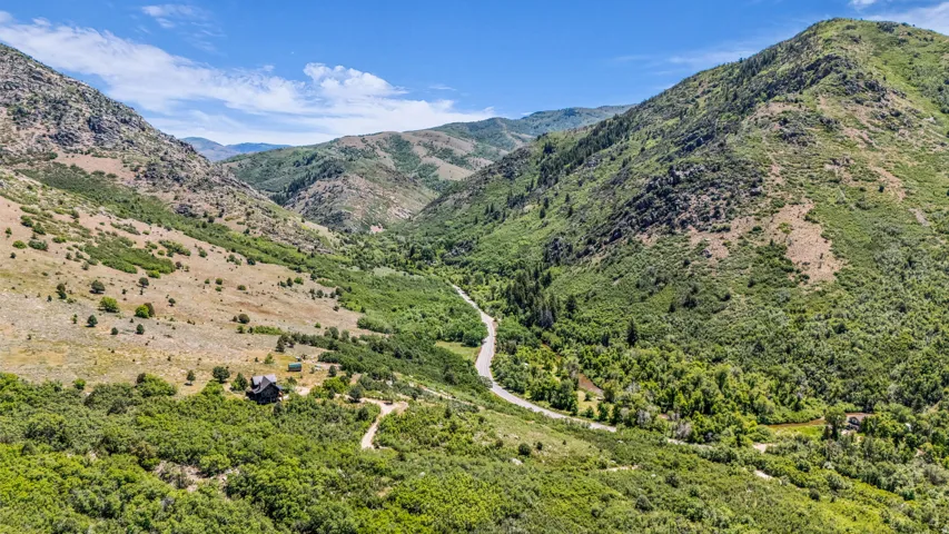 Mountain landscape with a winding road and a single structure nestled among lush green foliage