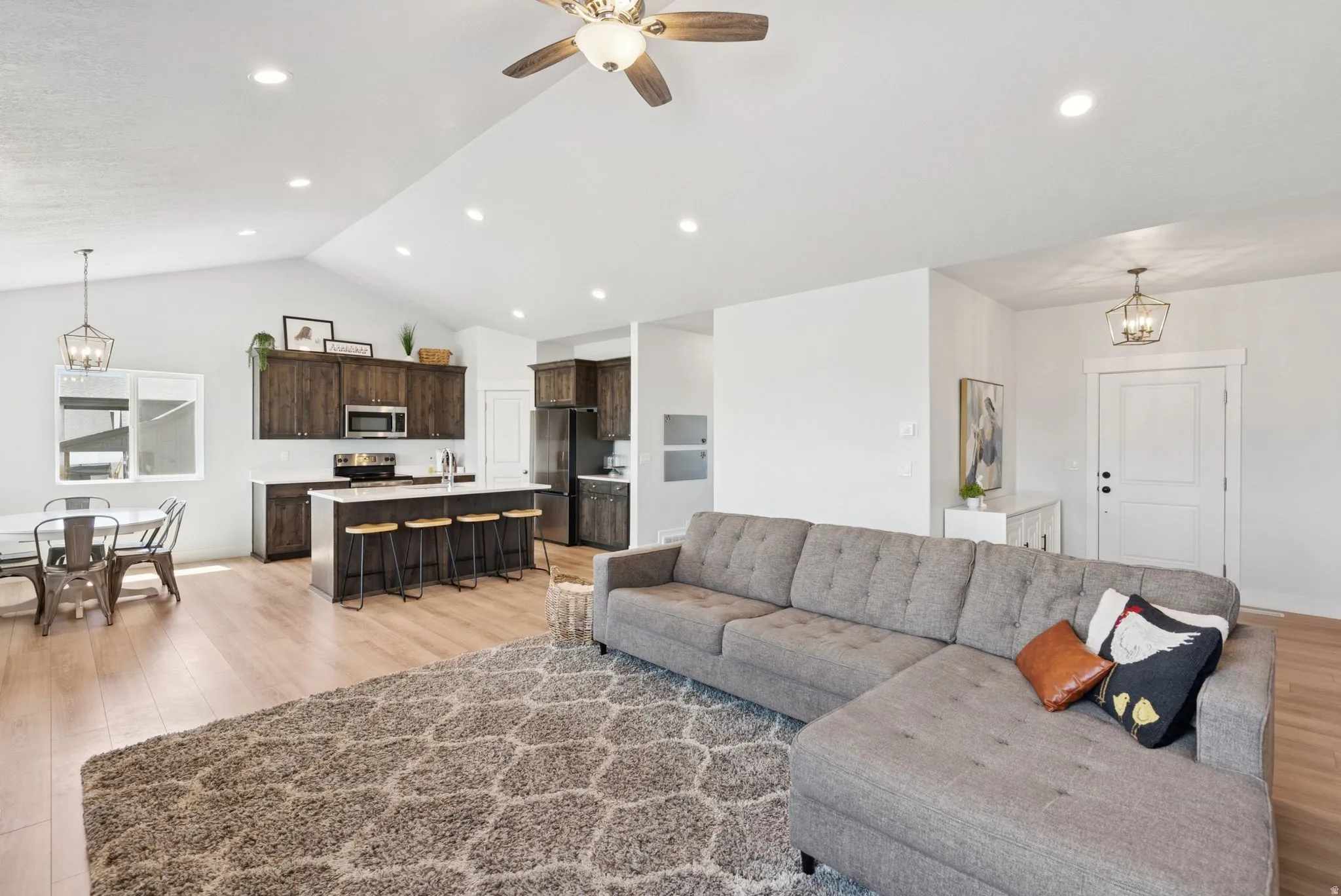 Open-concept living space featuring vaulted ceilings, wood-finish flooring, recessed lighting, and a ceiling fan