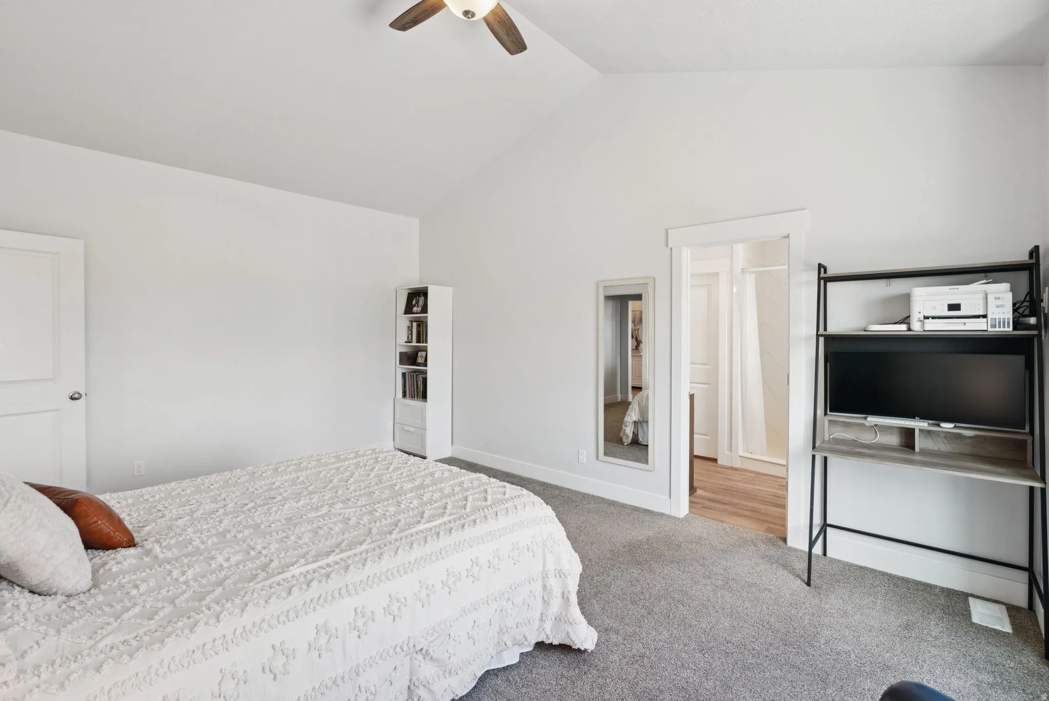 Vaulted ceiling bedroom featuring carpeting, a ceiling fan, and a doorway opening to a bathroom with wood-finish flooring