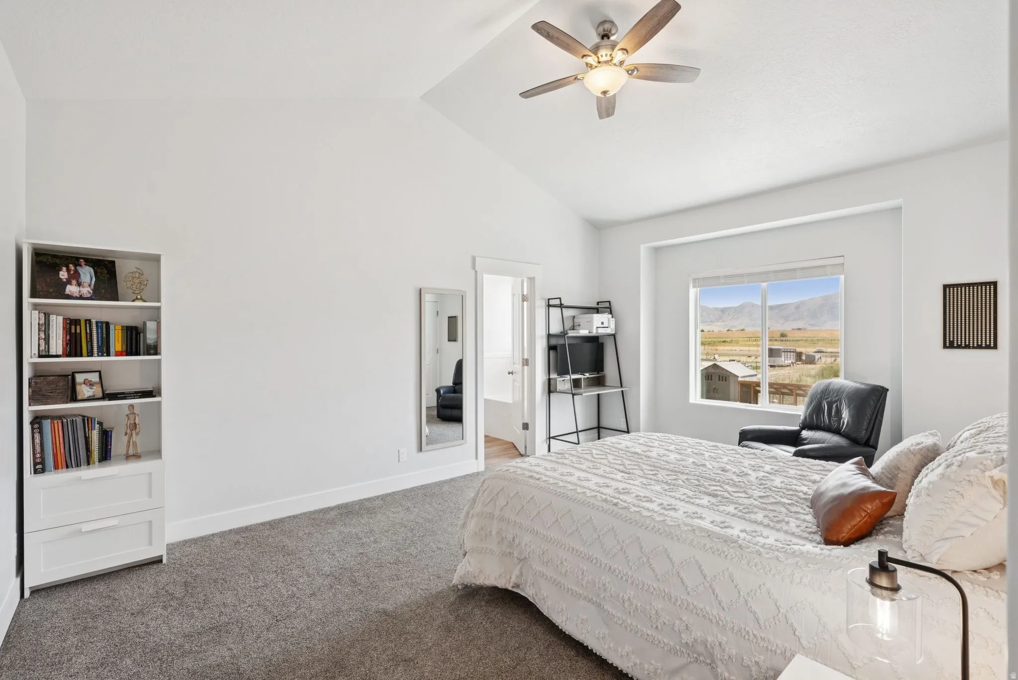 Spacious room featuring a vaulted ceiling with a ceiling fan, a large window with distant mountain scenery, and plush grey carpeting
