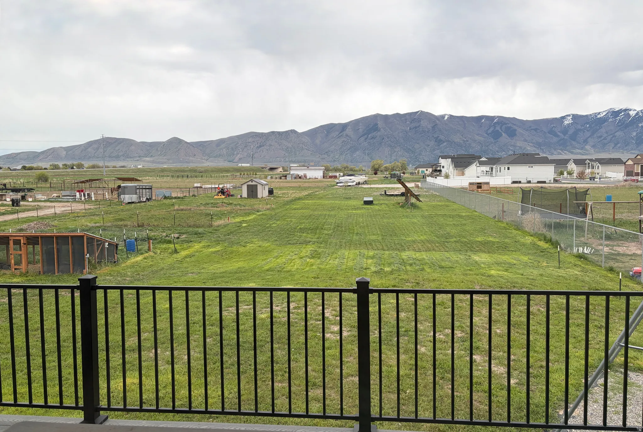 Spacious green lot with mountain backdrop, bordered by a black metal railing
