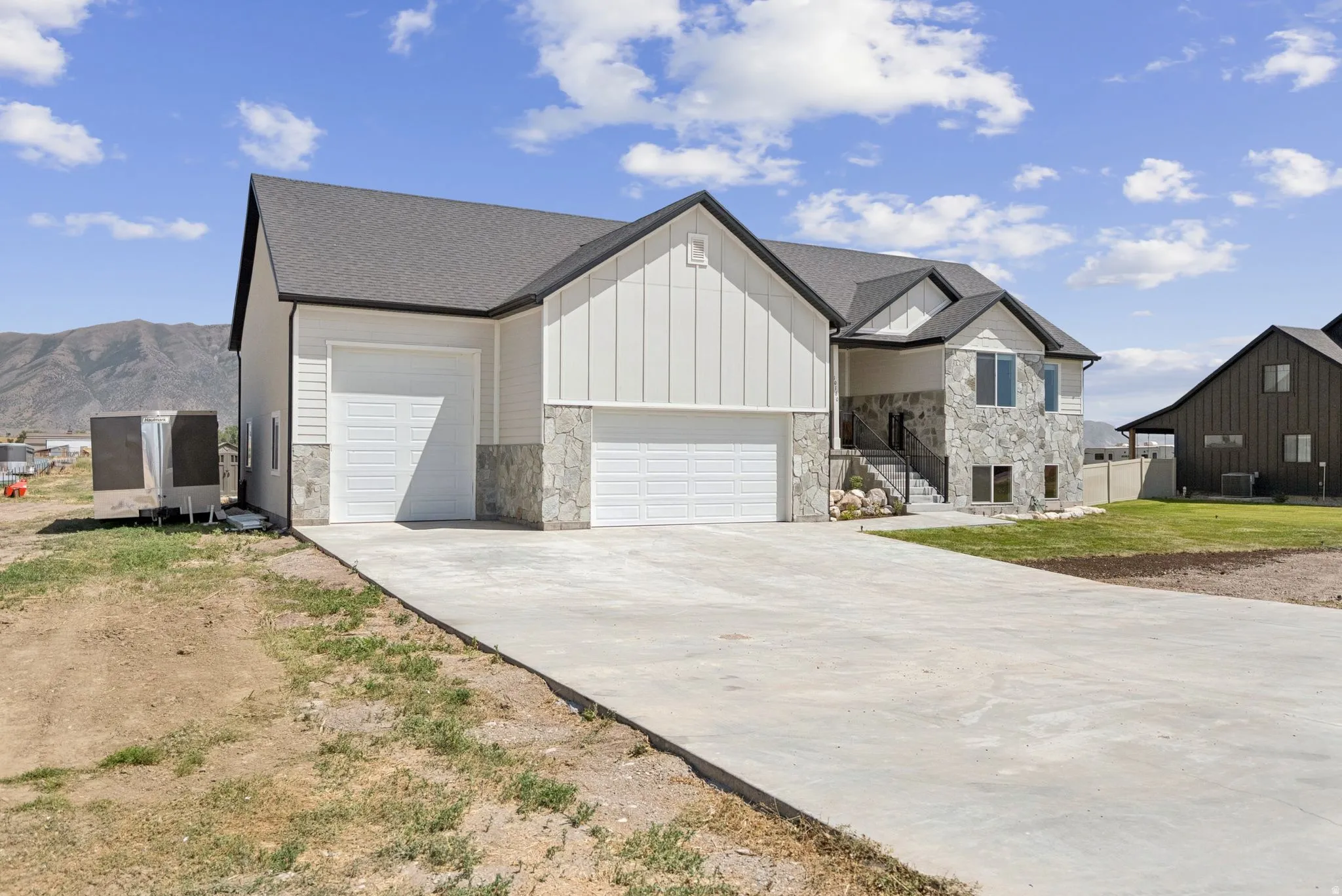 Exterior featuring a multi-tone stone and vertical siding facade, dark shingle roofing, a two-car garage, and a concrete driveway