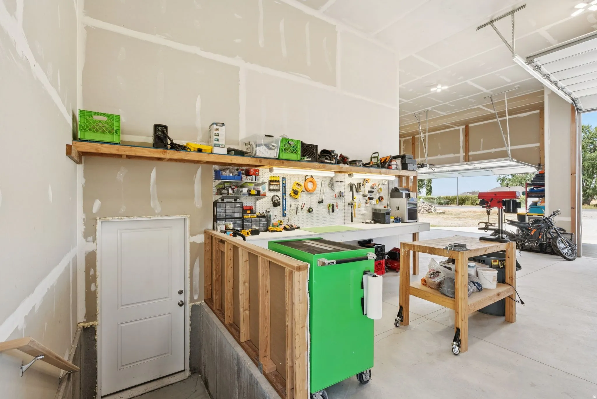 Spacious garage workshop featuring a large overhead door, concrete flooring, built-in shelving, and a dedicated workspace