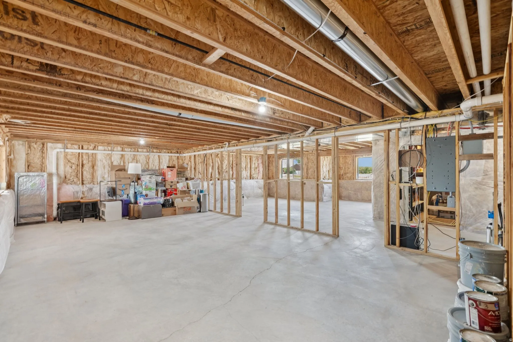 Unfinished basement with exposed wood joists and subflooring, framed wall sections, and a concrete slab floor