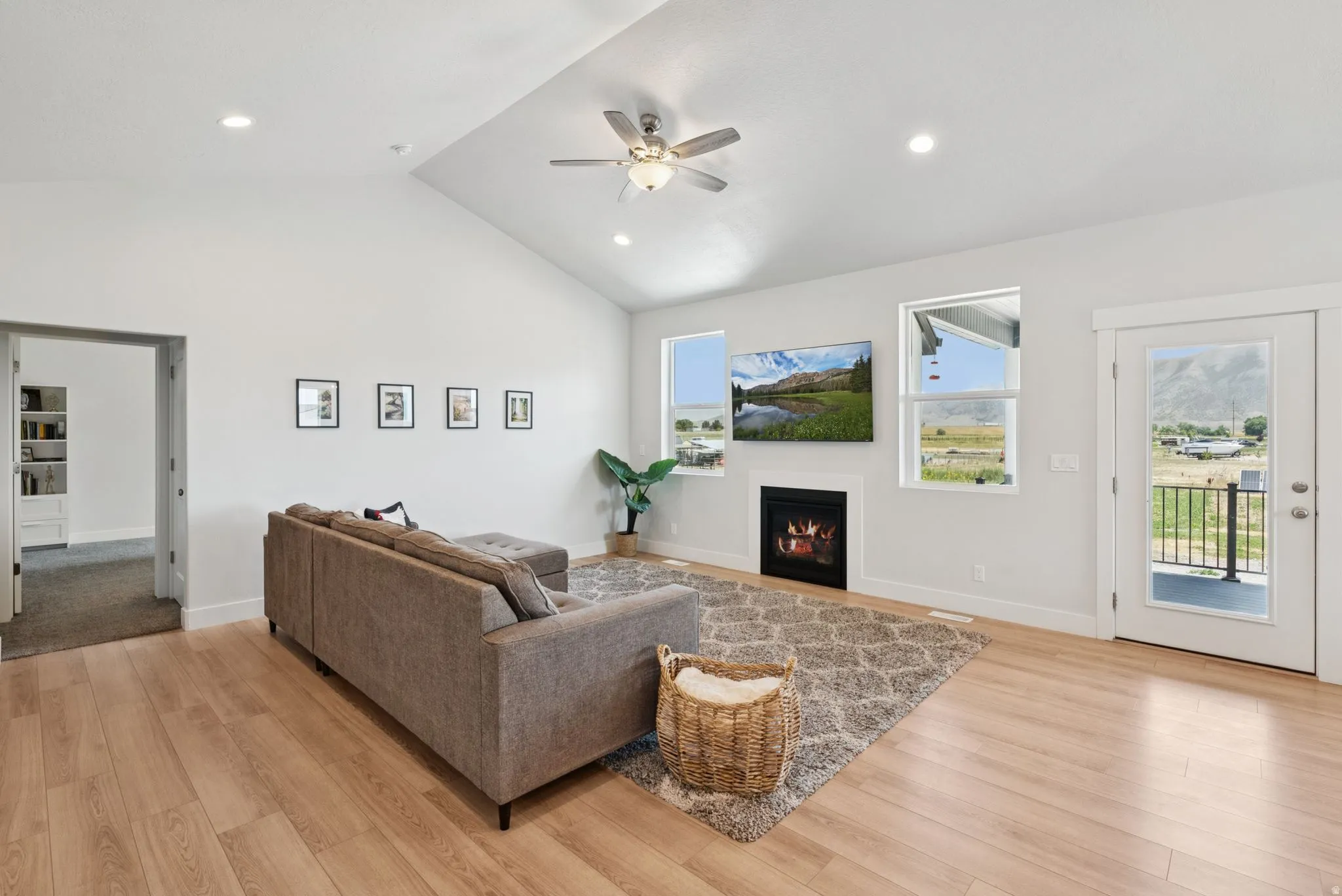 Spacious living area featuring light wood-finish flooring, vaulted ceilings with recessed lighting, and a ceiling fan