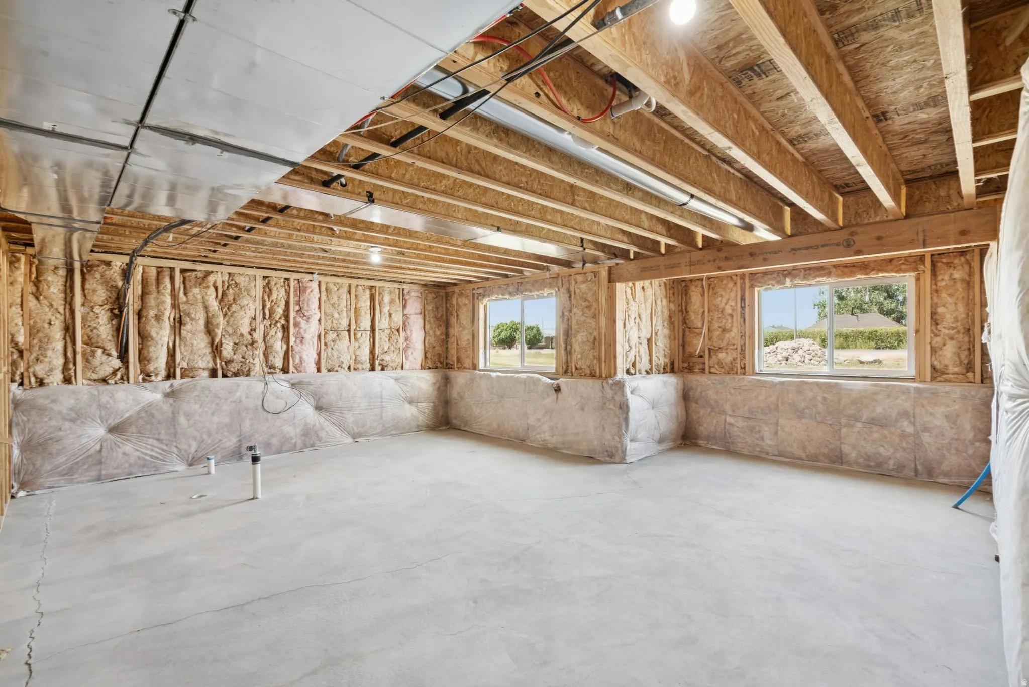 Unfinished basement space featuring exposed wood framing, concrete flooring, two windows, and visible insulation