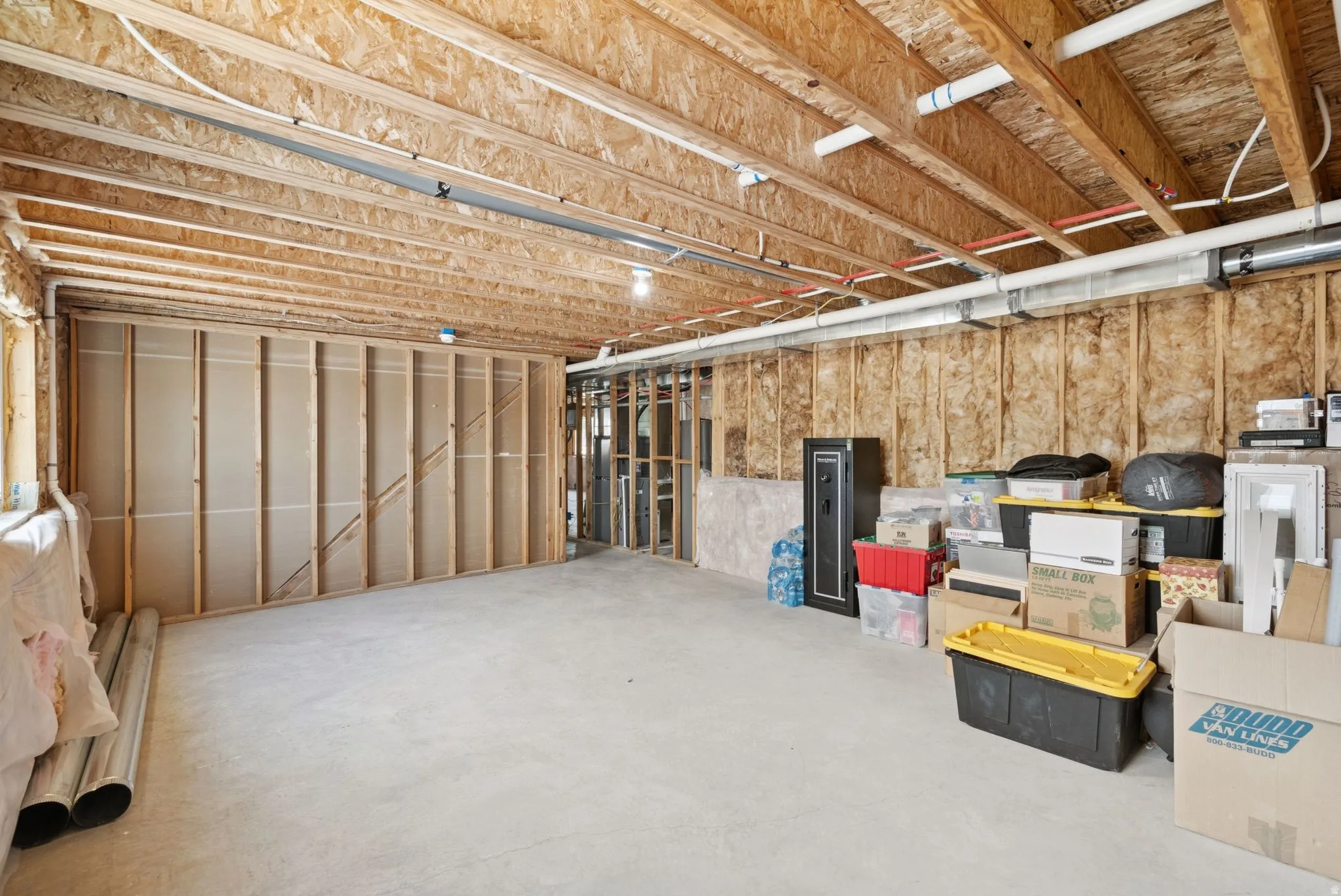 Unfinished basement featuring exposed wood joists, concrete flooring, and framed wall sections