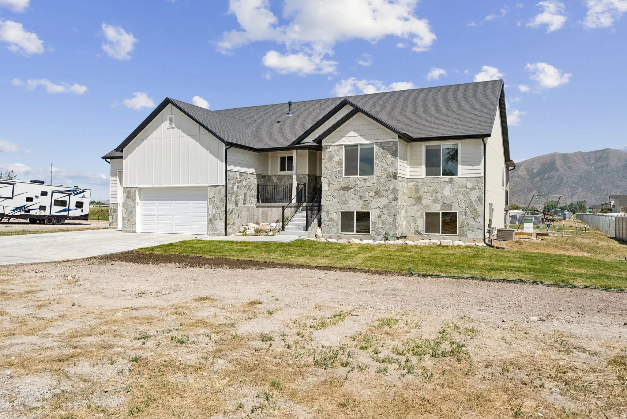 Modern split-level residence featuring a two-car garage, partial stone veneer, horizontal siding, vertical board and batten siding, and a concrete driveway
