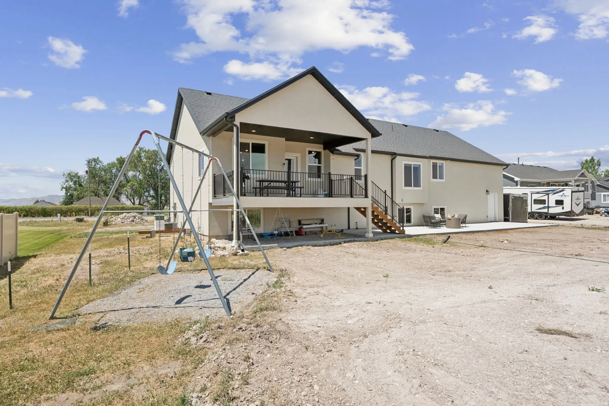 Rear exterior featuring a covered balcony with black railings, ground-level patio space, and a gravel-covered area