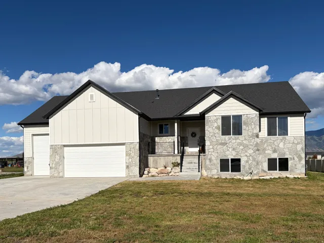 Contemporary two-story residence featuring a stone and siding exterior, multi-car garage, covered porch entry, and a dark shingle roof
