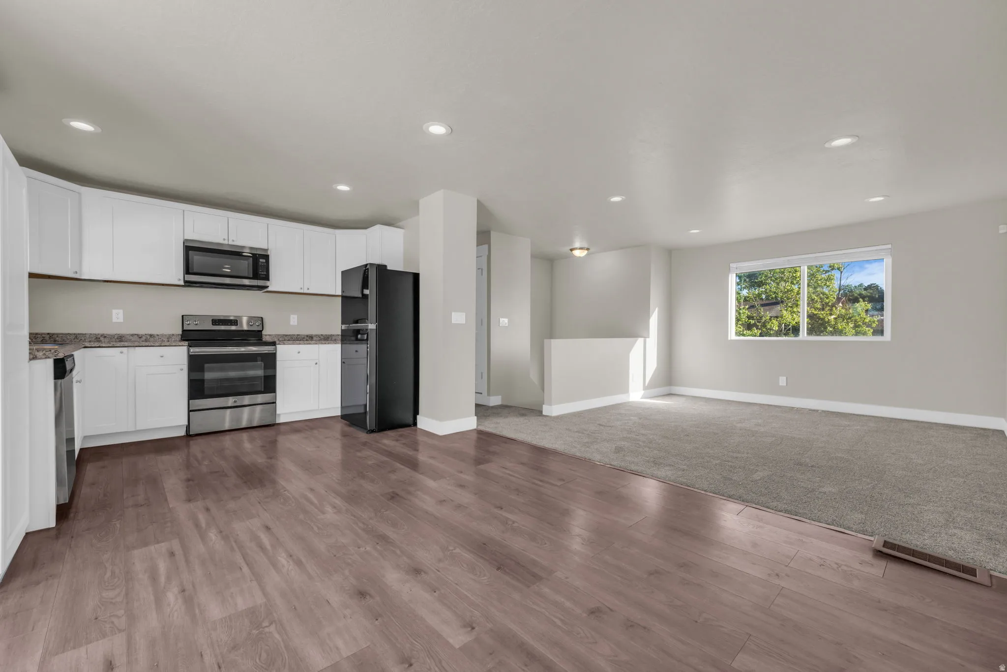 Open-concept living space featuring a modern kitchen with white cabinetry, stainless steel appliances, and wood-finish flooring