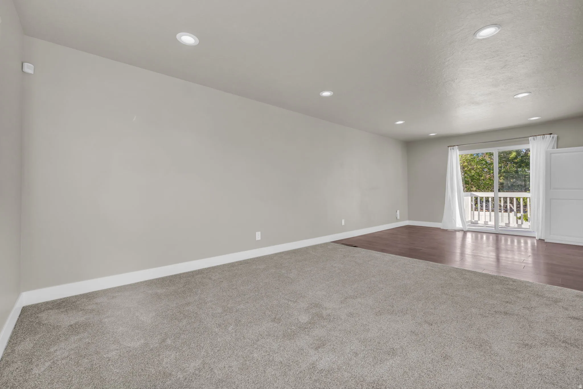 Spacious room featuring light gray walls, recessed lighting, and a blend of gray carpeting and wood-finish flooring