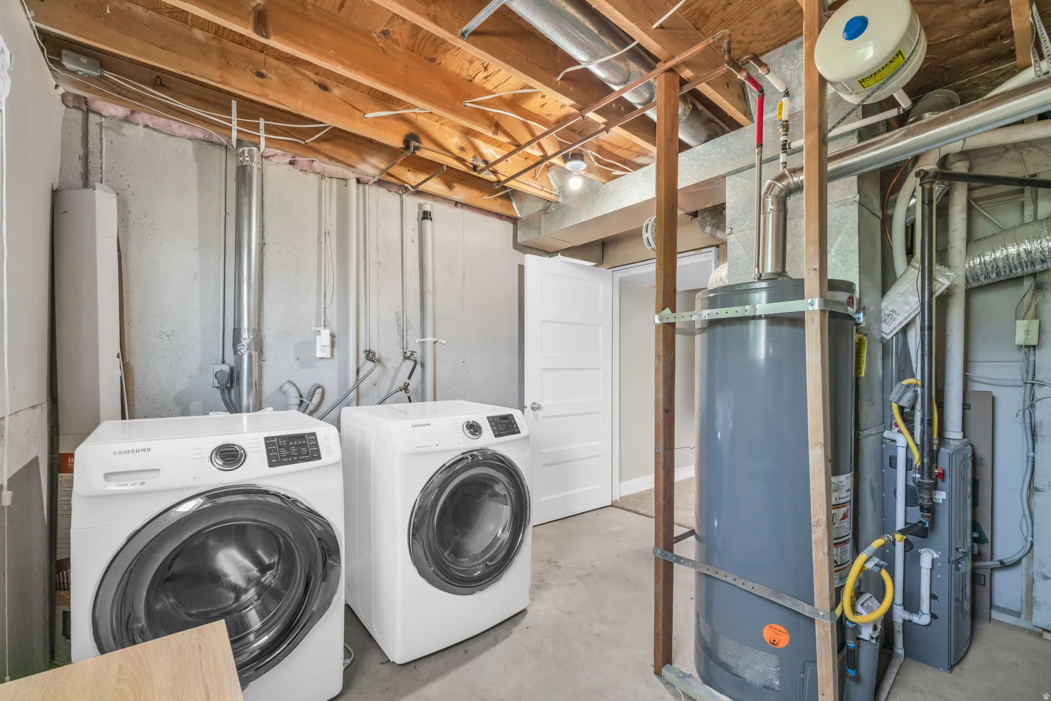 Utility area with exposed ceiling joists, concrete flooring, and a white interior door