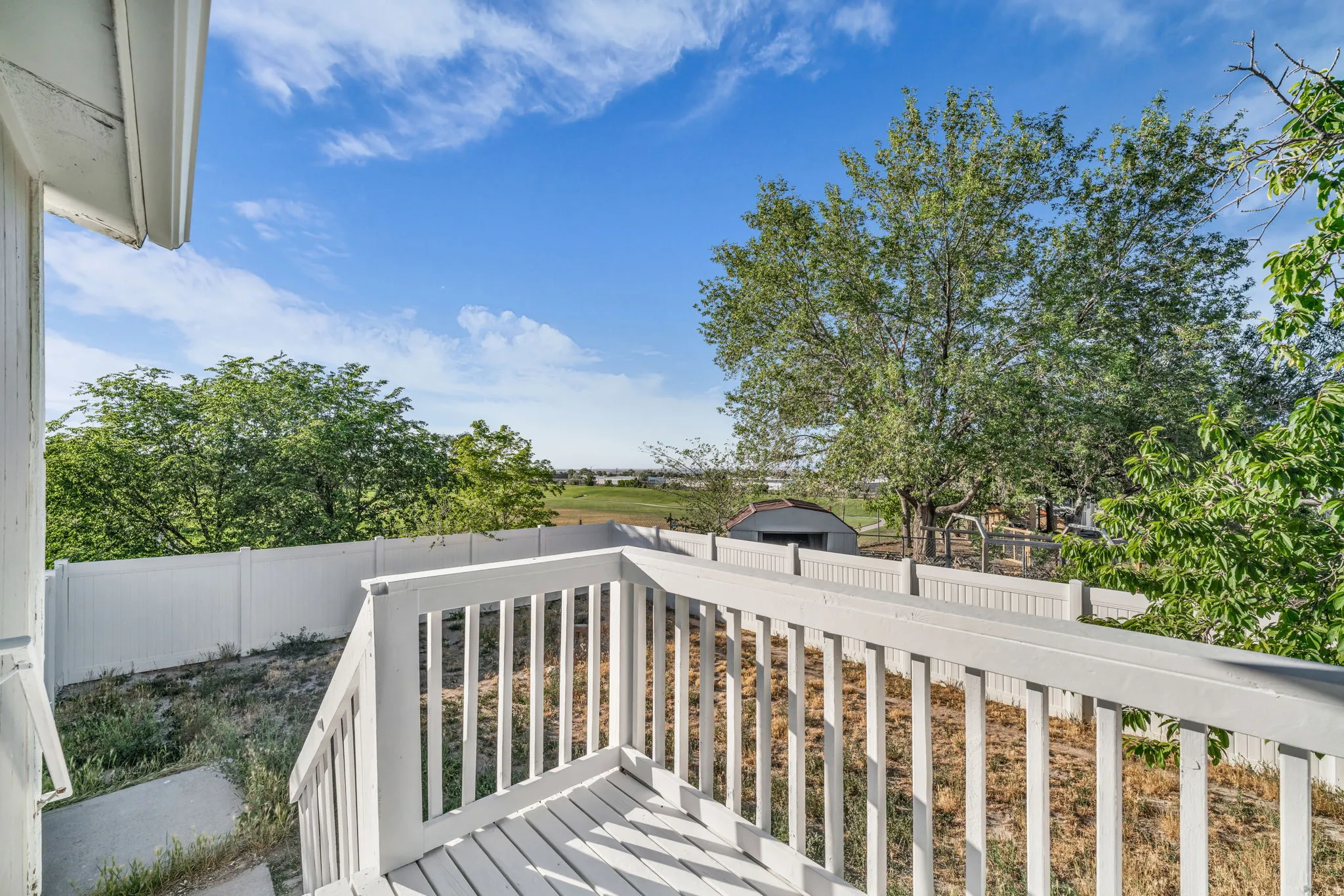 Outdoor deck area with white railings, a white privacy fence, and mature trees