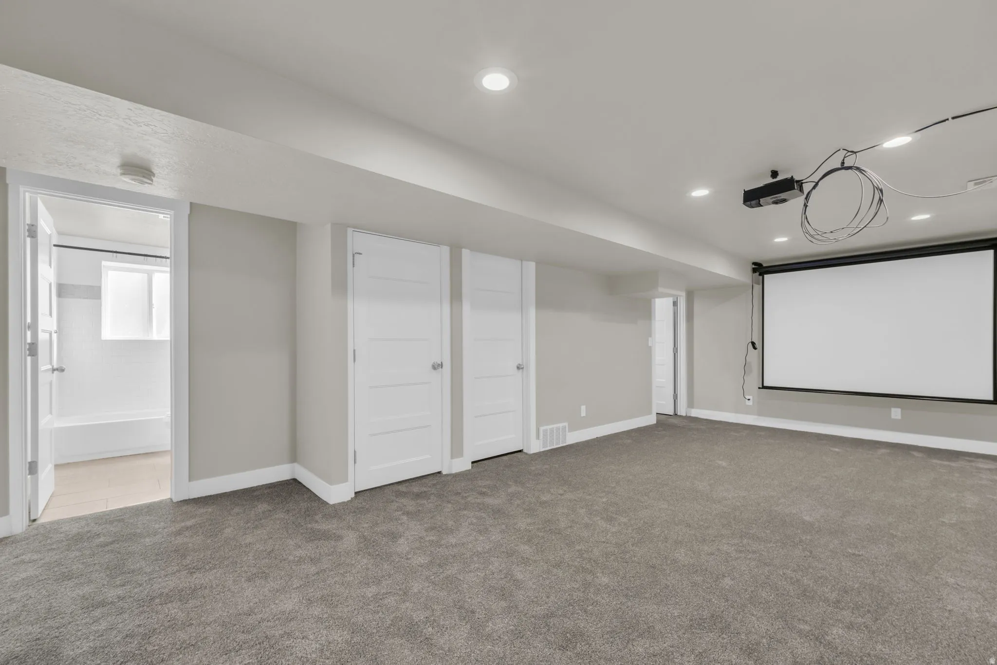 Spacious room featuring neutral carpeting, recessed lighting, and a projector with a pull-down screen