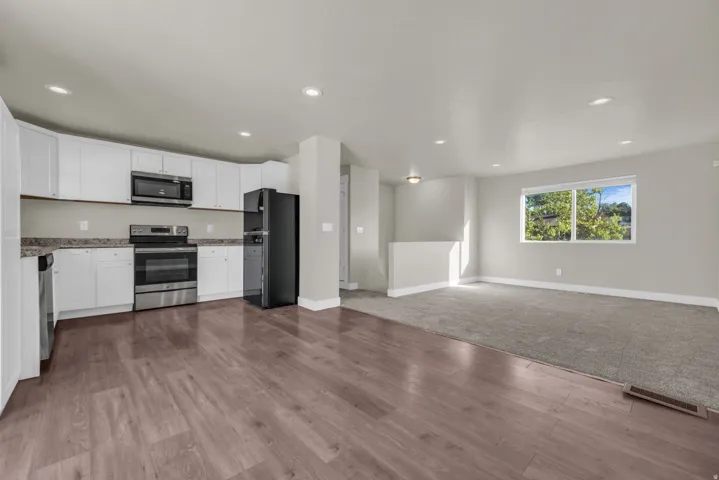 Open-concept living space featuring a modern kitchen with white cabinetry, stainless steel appliances, and wood-finish flooring