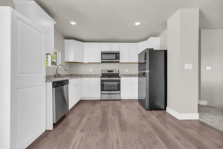 Modern kitchen featuring white cabinetry, stone-finish countertops, stainless steel appliances, and wood-finish flooring