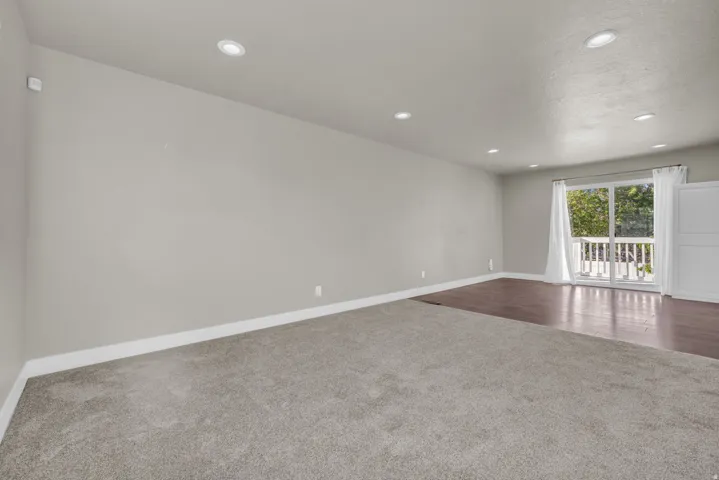 Spacious room featuring light gray walls, recessed lighting, and a blend of gray carpeting and wood-finish flooring