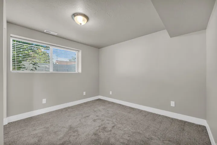 Room featuring neutral wall paint, gray carpet flooring, white baseboards, and a single window with horizontal blinds