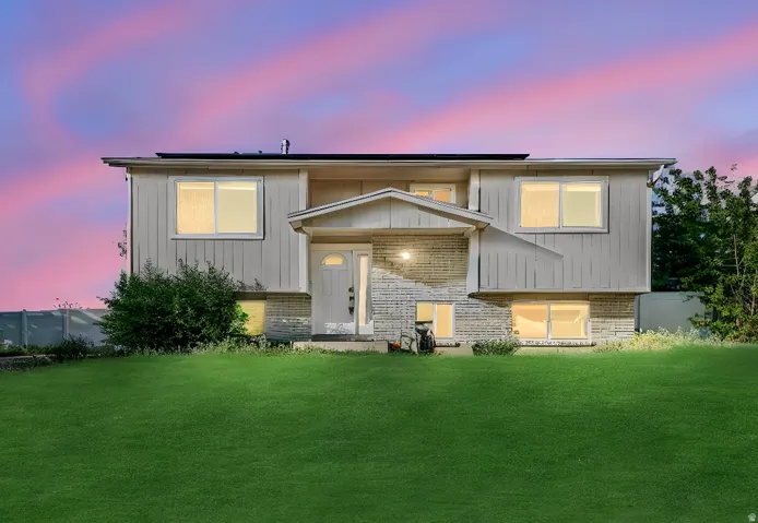 Split-level residence featuring a brick and vertical siding exterior, a front entry with a transom window, and a prominent front lawn