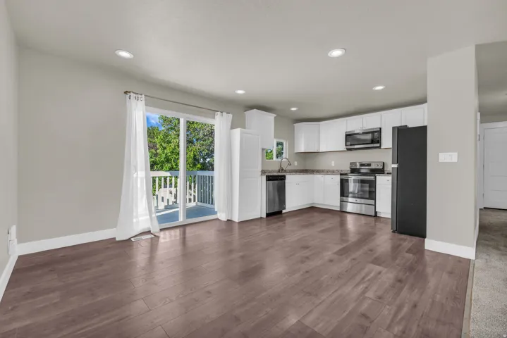 Open-concept kitchen and living area featuring wood-finish flooring, white cabinetry, stainless steel appliances, and recessed lighting
