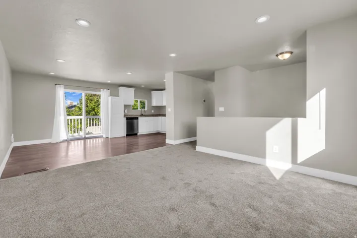 Open-concept living area featuring light gray walls, recessed lighting, and a blend of gray carpet and wood-finish flooring